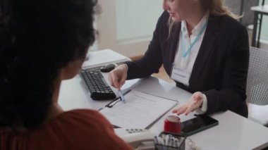 Kafkasyalı sosyal hizmetler görevlisinin sosyal hizmetlerdeki kadın müşteriye evrakları açıklarken ki görüntüsünü kaldır.