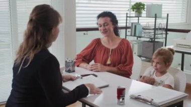 Modern ofiste küçük bir kızın annesine rehberlik eden kadın sosyal danışmanın orta boy fotoğrafı.