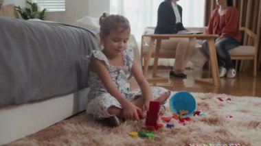 Annesi arka planda sosyal hizmet görevlisiyle konuşurken küçük bir kızın oyuncaklarla oynadığı geniş açı.