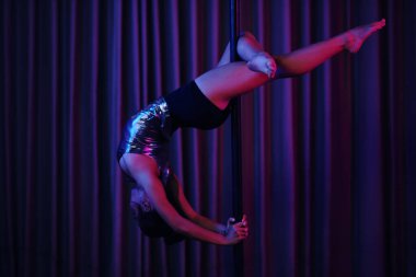 Polonyalı dansçı zarif bir şekilde loş odada metalik kıyafetlerle perde arkasını göstererek dinamik ve zarif bir performans ortamı yaratıyor.