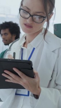 Beyaz önlüklü genç beyaz kadın pratisyen hekimin tıp konferansını ziyaret edişinin dikey çekimi.