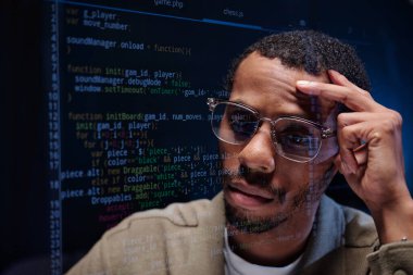 Gözlük takan adam karanlık odada çalışırken lenslere yansıyan bilgisayar kodlarını analiz etmeye odaklanmış. Kod ve teknik detaylarla dolu arkaplan yoğun bir ayar oluşturuyor