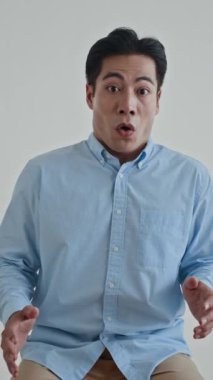 Asyalı adamın beyaz arka plandaki kameraya bakarken şok geçirdiği dikey çekim.