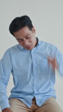 Gündelik gömlekli genç adamın dikey stüdyo çekimi beyaz arka planda kızgınlığını ifade ediyor.