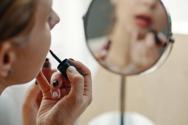 Kadın aynanın karşısına dikkatlice ruj sürüyor, makyajını mükemmelleştirmeye odaklanıyor. Yansıma, elinde ruj aplikatörü tutarken niyetinin ne olduğunu gösteriyor.