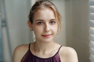 Hoş bir gülümseme ile kameraya bakan kadın portresi, günlük kıyafetler giyiyor ve kapalı bir yerde oturuyordu. Etrafı renkli bir çevreyle çevriliydi.