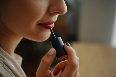 Close-up image of a woman carefully applying lip gloss with precision, highlighting delicate features. Soft background adds elegance to focus on beauty ritual clipart