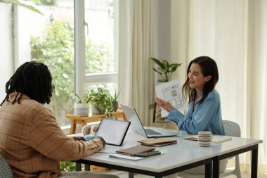 Çok ırklı meslektaşlar, modern bir ofis masasında dizüstü bilgisayarlarla verimli tartışmalara giriştiler. Büyük pencerelerden akan doğal ışık davetkar bir atmosfer yaratıyor.