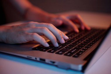 Bilgisayarın klavyesinde loş ışıklandırılmış şekilde yazı yazan insanların yakın görüntüsü, modern çalışma alanındaki iş ve teknolojiye odaklanma