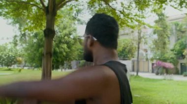 Aktif giyimli genç Hintli adamın şehir parkında kollarını kaldırıp kafa sallarken orta boy bir fotoğrafı.