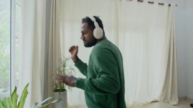 Evde kulaklıkla müzik dinlerken günlük kıyafetlerle dans eden Asyalı bir adamın el kamerası görüntüsü.