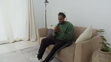 Erkek profesyonel dansçının oturma odasında kablosuz kulaklıkla müzik dinlerken elde çekilmiş bir fotoğrafı.