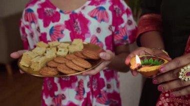Hint kıyafetleri içinde, Diwali sırasında ellerinde kurabiye ve yanan mumlarla tanınamaz bir anne ve kızın görüntüsü.