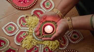 Rangoli 'nin yukarısında Diwali' de elinde yanan para tutan tanınmayan Hintli kadının elleri.