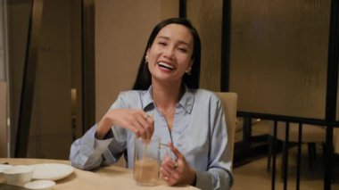 Genç Asyalı bir kadının kokteyl içerken ve trend bir restoranı ziyaret ederken kamerayla konuşurken ki görüntüsü.