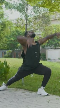 Şehir parkında antrenman yapan, esneyen ve hamleler yapan genç adamın dikey çekimi.