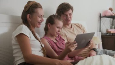 Kafkas kökenli neşeli ebeveyn ve kızın evde dinlenirken dijital tablet kullanarak eğlendiği orta boy bir fotoğraf.