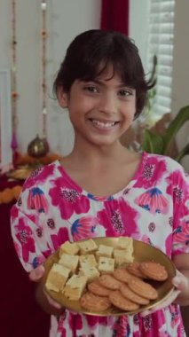 Çiçekli elbise giyen, Diwali 'de şeker taşıyan ve kameraya gülümseyen Hintli kızın dikey portresi.