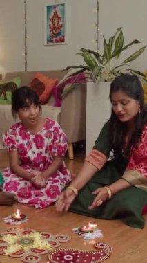 Diwali 'de yanan parayla Rangoli yaparken Hintli ailenin yan yana oturduğu dikey çekim.