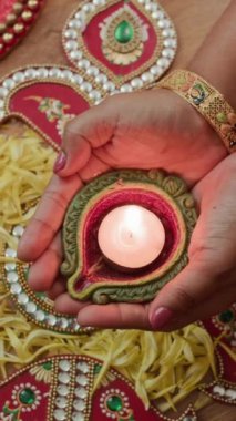 Diwali kutlamaları sırasında Rangoli üzerinde yanan para tutan kimliği belirsiz bir kadının dikey resmi.