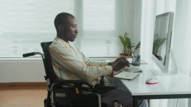 Modern ofis masasında çalışan Afrikalı Amerikalı erkek çalışanın geniş açılı görüntüsü.
