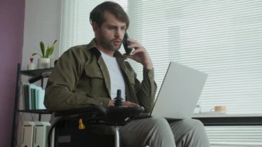 İş yerinde laptopunu kontrol ederken tekerlekli sandalyedeki ciddi beyaz iş adamının telefon konuşması...