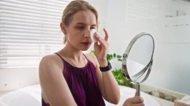 Kafkasyalı genç bir kadının evine aynaya bakarken pamuk yastıkla cilt bakımı yaparken yüzünü temizlemesi.