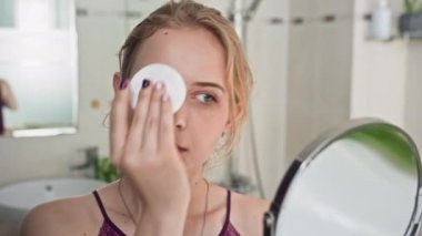 Banyoda aynaya baktığında yüzünü temizlerken pamuk ped kullanan Z jenerasyonundaki kadını kapat.