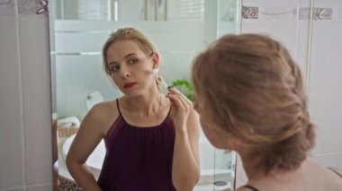 Banyoda aynanın önünde yuvarlanan beyaz bir kadınla yüz masajı yapan genç bir kadının omuzlarının üstünden.