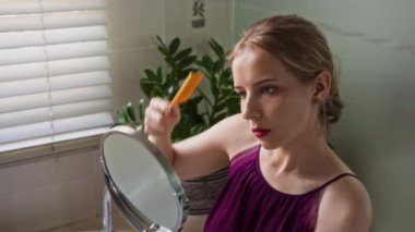 Kafkas kökenli bir kadının banyoda aynaya bakarken saçlarını taramasının yüksek açılı görüntüsü.