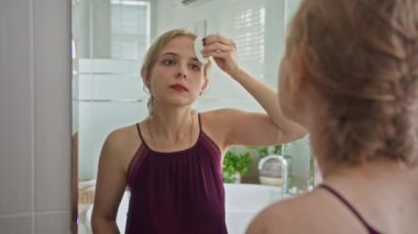 Banyoda aynanın önünde dikilirken yüzü pamukla temizleyen Kafkas genli Z kızının omuz manzarasından.