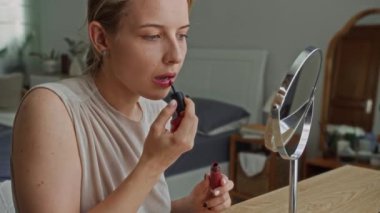 Kafkas kökenli orta boy kadın zoomcusu aynanın karşısında otururken evde kırmızı ruj sürüyor.