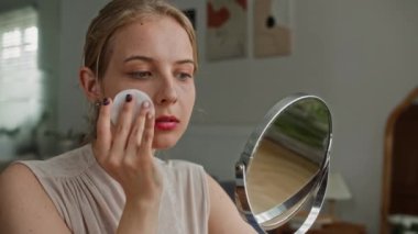 Beyaz ırktan Z genli bir kadının yatak odasına makyaj yapmadan önce yüzünü temizlerken pamuk ped kullanırken orta boy fotoğrafı.