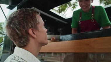 Z jenerasyonundaki adamın Asyalı yemek kamyonu işçisine sandviçlerin içeriğini sorduğu el kamerası görüntüsü.