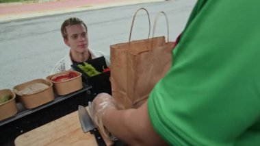 Beyaz ırktan genç bir adamın sokak aşçılığı satın alıp yemek kamyonundan siparişini alırken elde çekilmiş bir fotoğrafı.