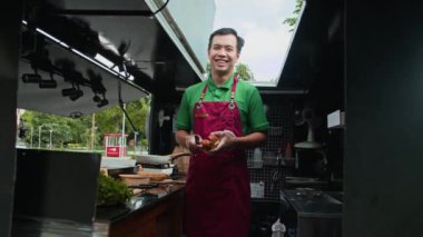 Neşeli Asyalı yemek kamyonu sahibinin düşük açılı portresi müşteriler için taze sandviç pişiriyor ve kameraya gülümsüyor.