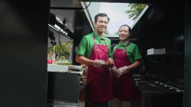 Kameraya gülümseyen, üniformalı, neşeli Asyalı yemek kamyonu sahiplerinin düşük açılı portresi.