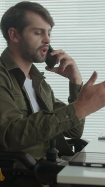 Engelli erkek yöneticinin kapalı bir ofiste çalışırken akıllı telefondan konuşma görüntüsü.