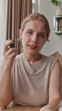 Genç Z blogcusunun dikey POV 'u evde otururken kamerada makyaj ürünleri hakkında konuşuyor