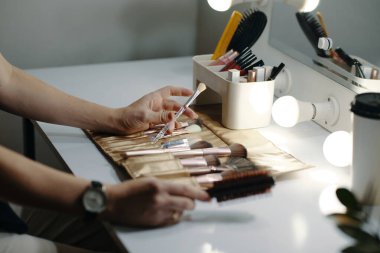 Makyaj çantasından makyaj fırçalarını seçen ellerin yakın çekimi makyaj organizatörleriyle birlikte makyaj masasında, devam eden güzellik rutini ve kişisel bakım hazırlıklarını yansıtıyor.