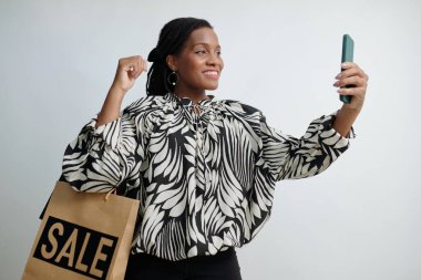 Yüzünde gülümsemeyle alışveriş torbası tutan bir kadın mutlu bir şekilde selfie çekiyor.