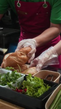 Tanımlanamayan sokak kafe çalışanının dikey görüntüsü. Ekmek ekmeğine dolgu malzemesi ekliyor.