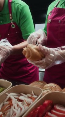 Üniformalı yemek kamyonu çalışanlarının ekmek çöreklerinden ve çeşitli dolgulardan sandviç yaparken dikey çekimleri.