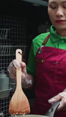 Genç Asyalı kadın yemek kamyonu satıcısının yemek pişirirken yumurta kızartırken dikey çekimi.