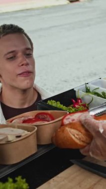 Kafkas kökenli genç bir adamın yemek kamyonundan malzeme alırken sandviçe malzeme eklemek istemesi dikey bir pozu.