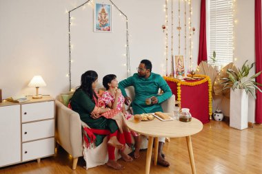 Family gathered cozying on sofa engaging in warm conversation during festivity. Lively decorations adorning wall and table, emphasizing cultural and seasonal celebration clipart