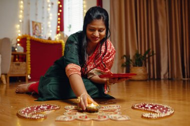 Geleneksel festival sırasında sanatsal açıdan Rangoli tasarımı yapan bir kadın. Dekoratif elementler aydınlatılmış arka planda şenlikli atmosfer oluşturur