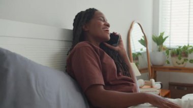Yatak odasında arkadaşınla konuşurken gülümseyen, gülen ve el kol hareketi yapan Afro-Amerikan genç bir kadın.