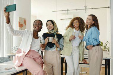 Günlük toplantılar sırasında iş yerinde kutlama yaparken selfie için poz veren dört farklı kadından oluşan bir grup. Herkes kadehini kaldırsın, şenliklerin tadını çıkarsın.