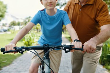 Dedem küçük torununa parkta bisiklet sürmeyi öğretiyor.